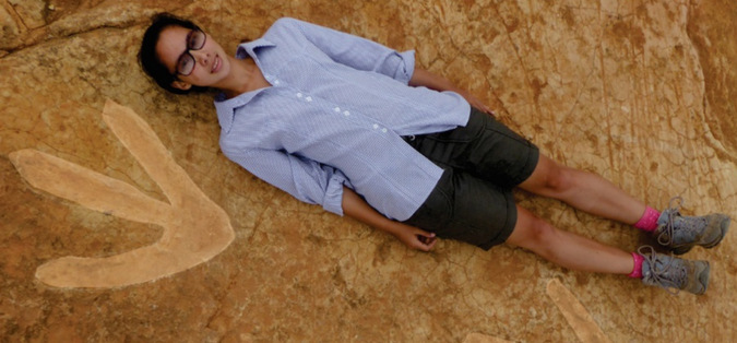 Researcher lying next to dinosaur footprint