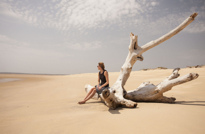 Person sitting on drift wood on empty beach in Lamu, Kenya