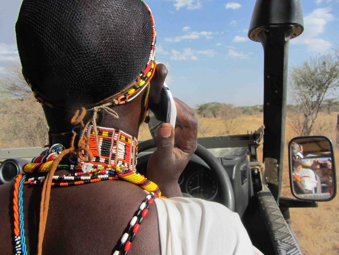 Maasai warrior with cellphone driving a game drive vehicle