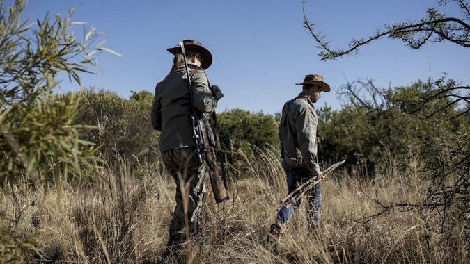 Two people in the African bush, one has a rifle