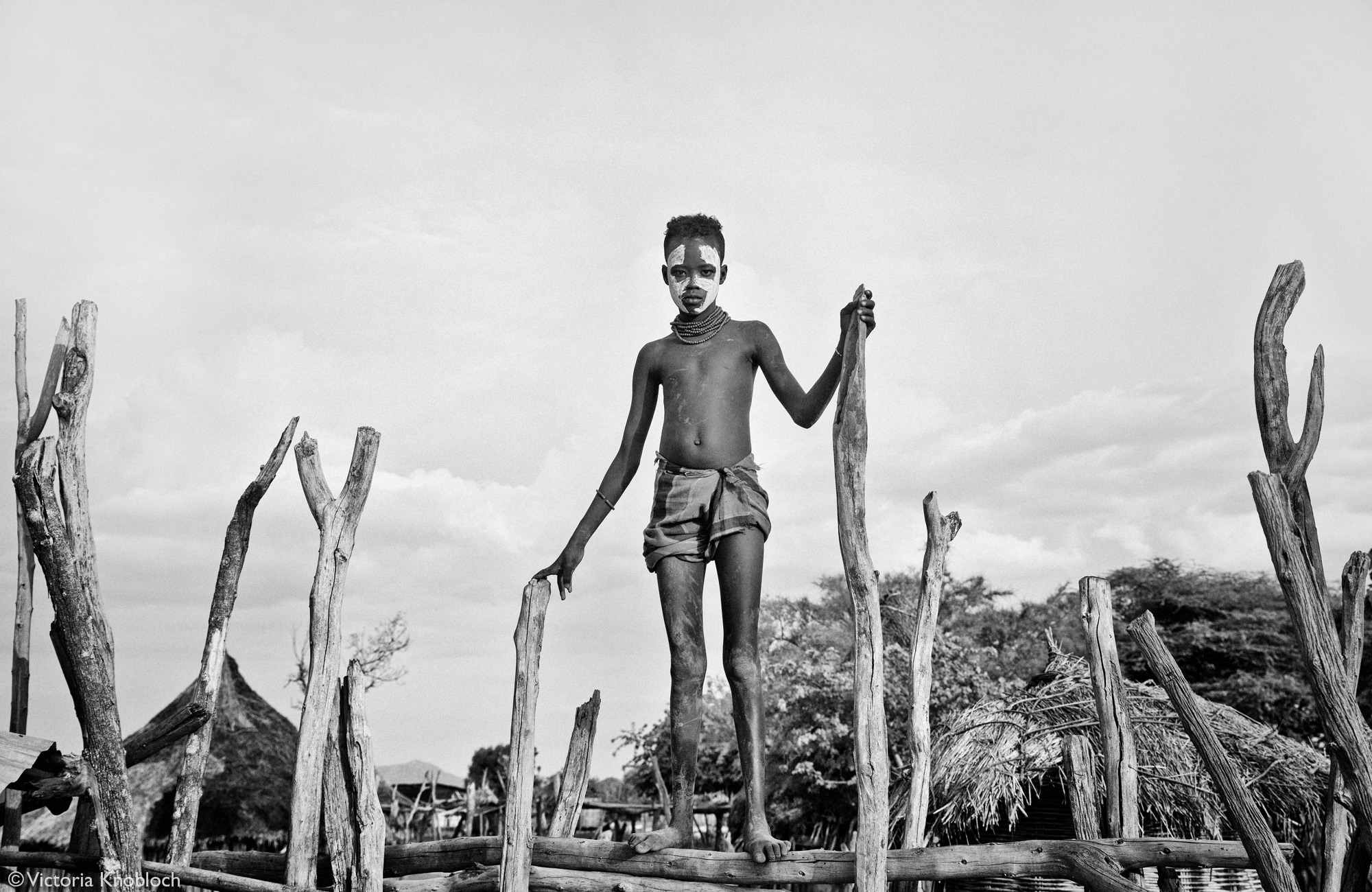 Karo tribe boy standing on top of wooden fence, Omo Valley, Ethiopia